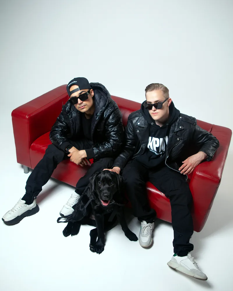 Dog Hustlers -DJ-duo punaisella sohvalla mustan koiran kanssa